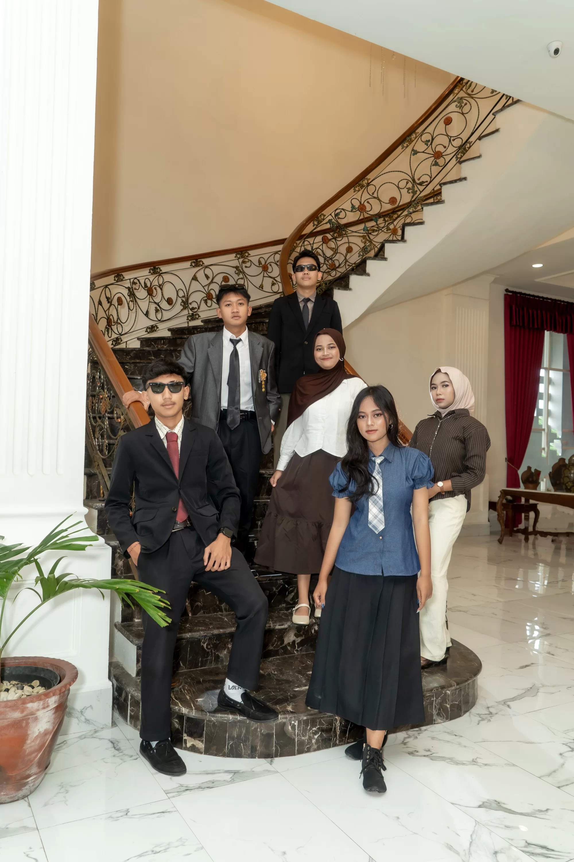 Sekelompok siswa berpose rapi mengenakan pakaian rajut turtleneck dan blazer klasik berlatar bangunan arsitektur kolonial
