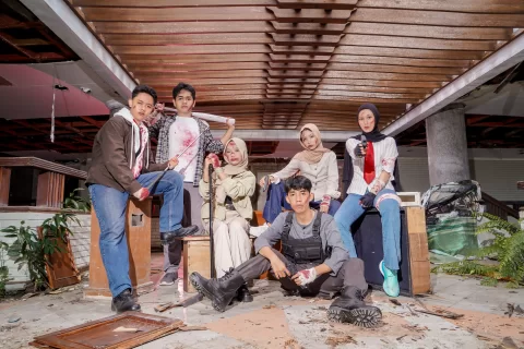 Sekelompok siswa berpose mengenakan rompi taktis dan perlengkapan agen dengan latar lorong laboratorium gelap