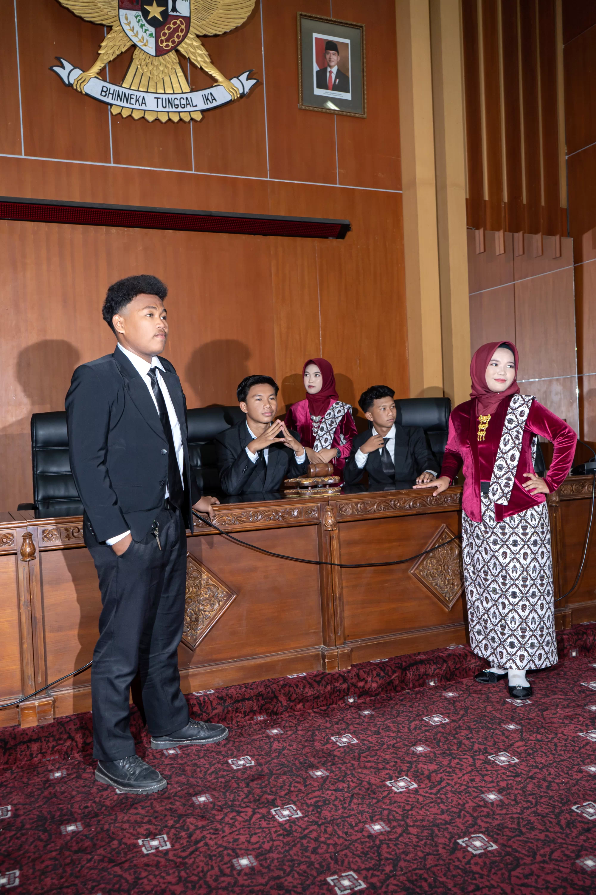Sekelompok siswa duduk di kursi ruang sidang legislatif dengan balutan jas formal, berpose seolah sedang melakukan rapat paripurna