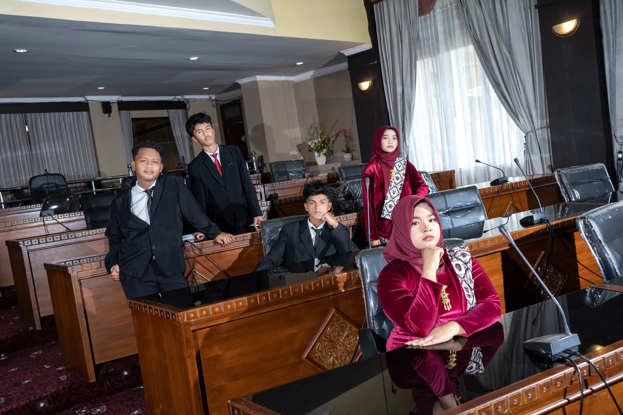 Potret tegas seorang siswa berdiri di podium ruang sidang dengan mikrofon menyampaikan aspirasi, dikelilingi rekan-rekan seangkatannya