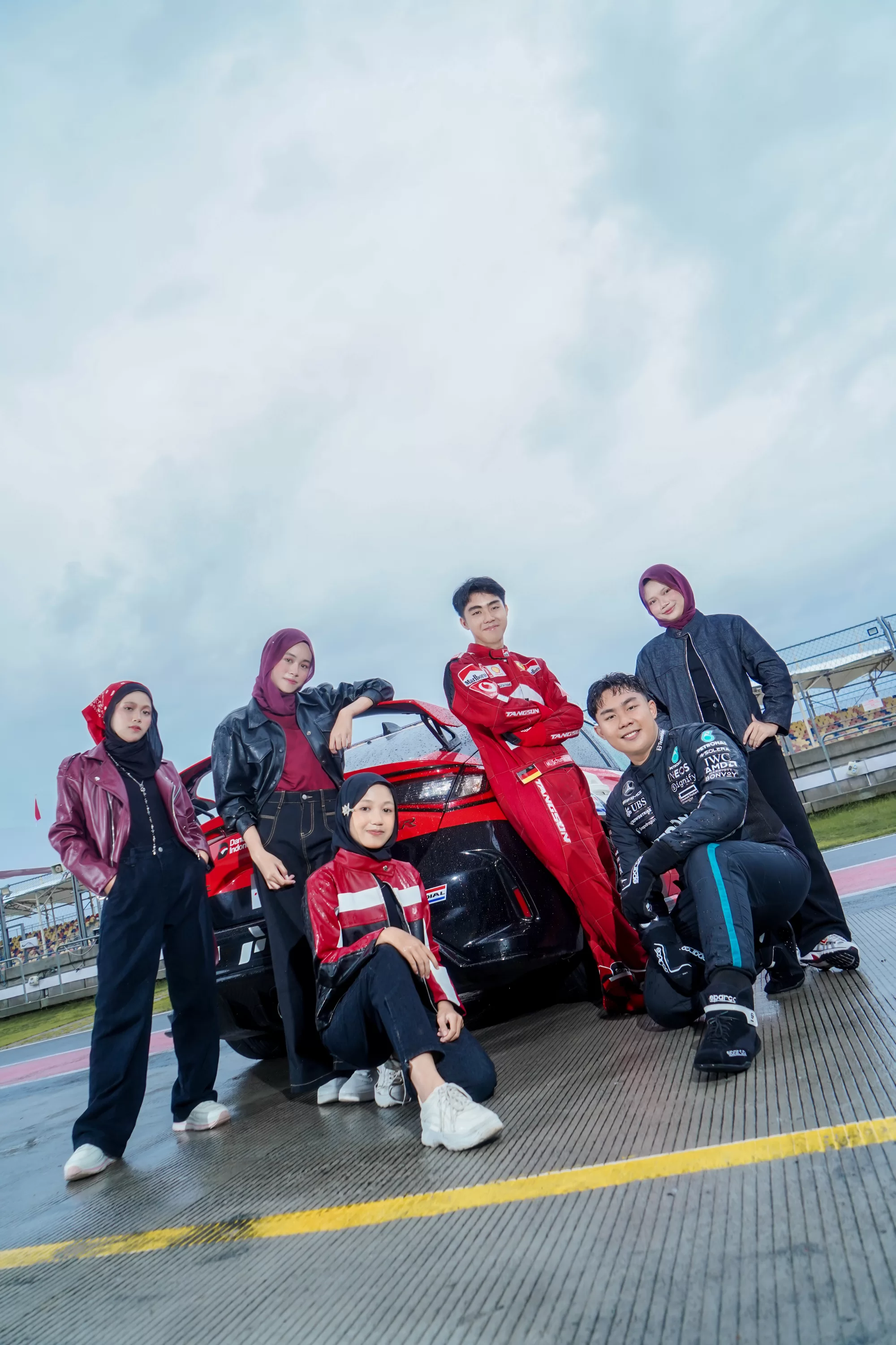 Sekelompok siswa berpose mengenakan jaket balap khas tim F1 dengan latar pit lane dan mobil balap
